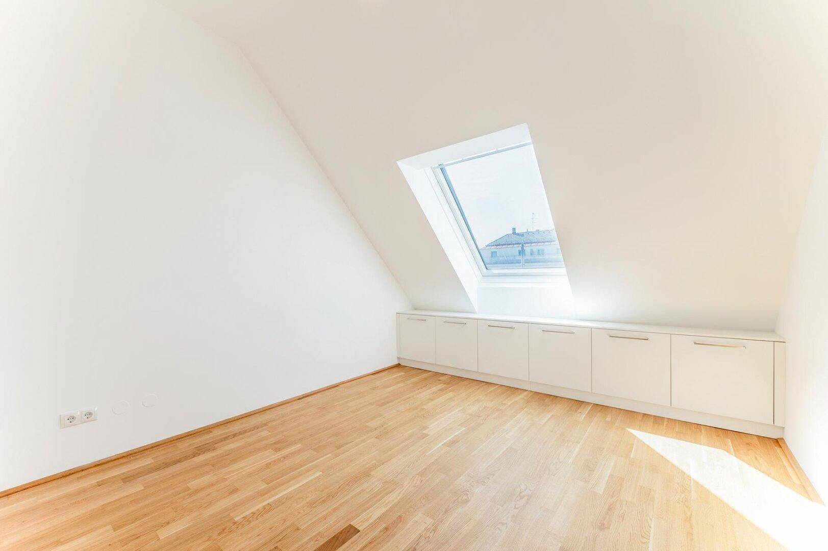 Heller Raum mit Holzboden, Dachschräge, Dachfenster und praktischen Einbauschränken unter der Schräge.