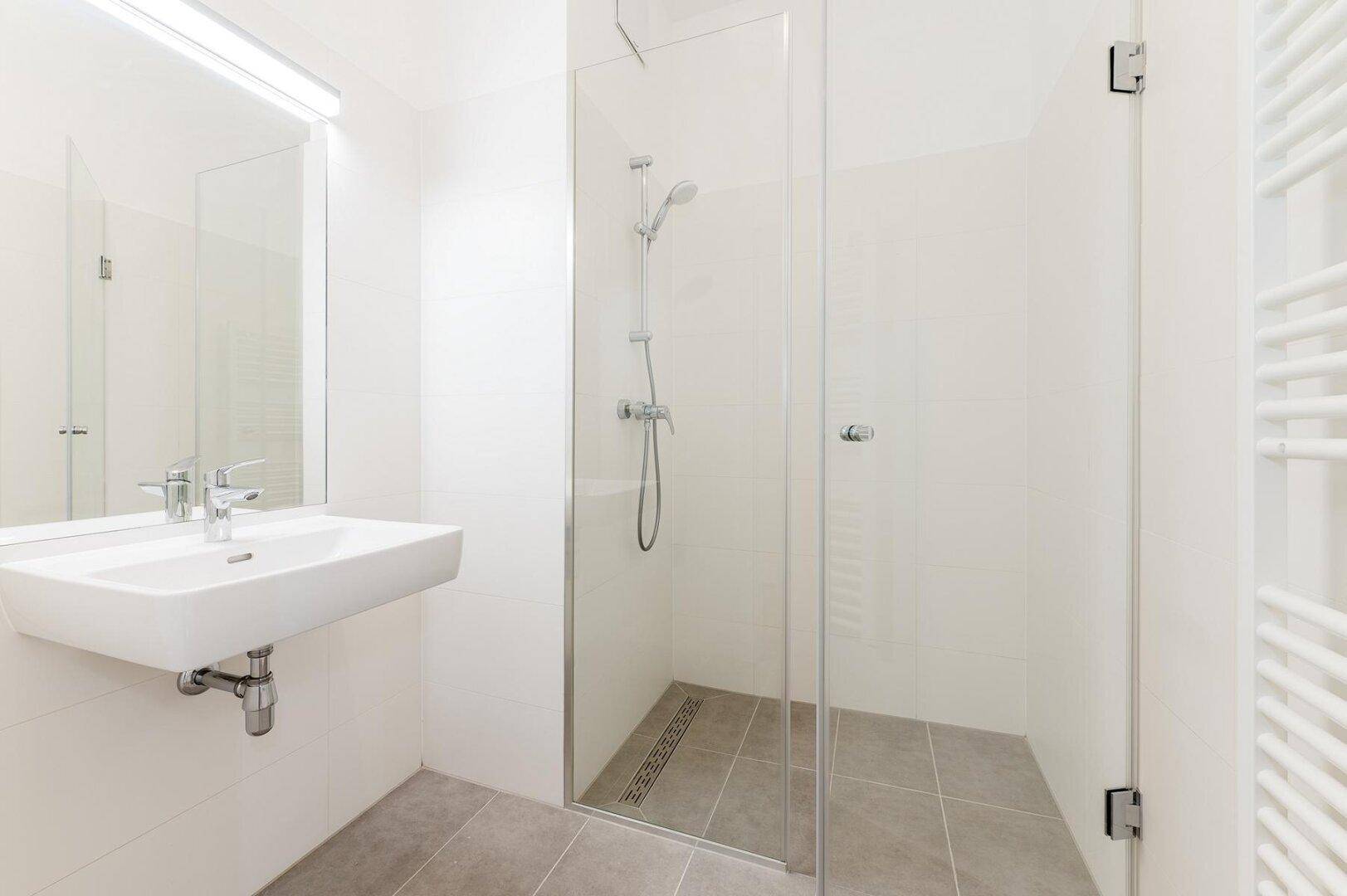 Modernes Badezimmer mit ebenerdiger Dusche, Einzelwaschbecken und beheiztem Handtuchhalter.