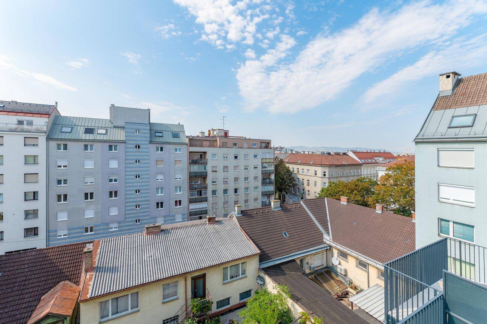 Ausblick über die Dächer der Stadt mit verschiedenen Wohngebäuden und einem weiten Himmel.