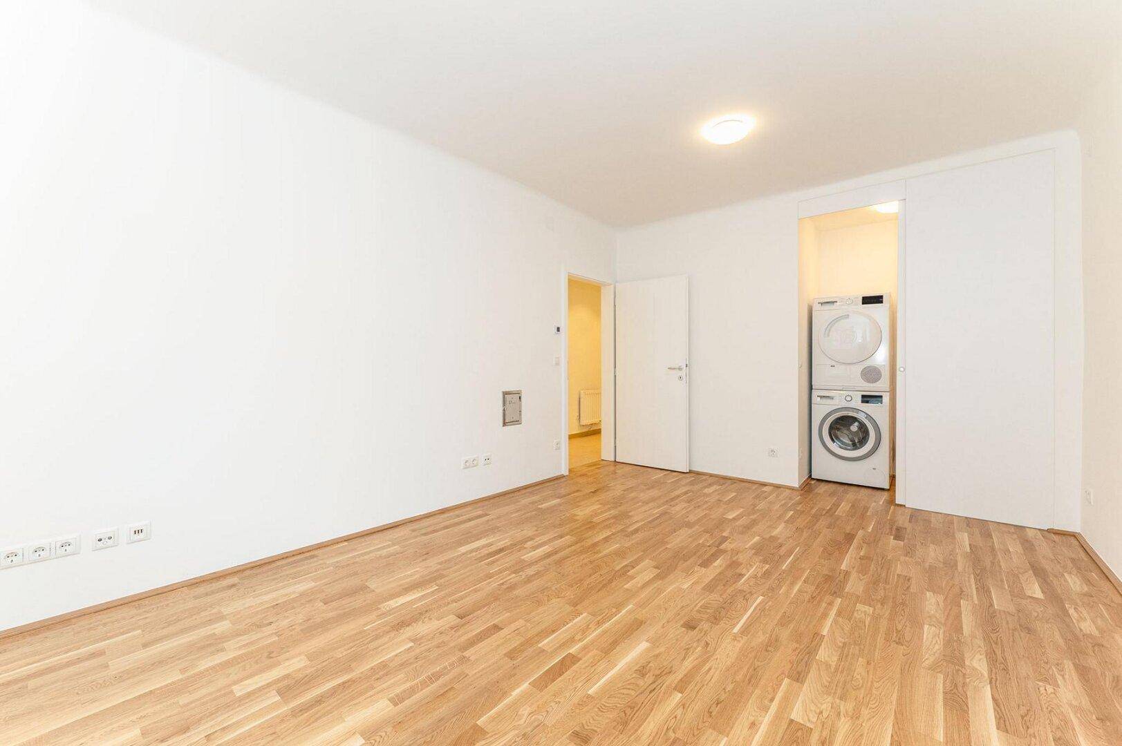 Heller Raum mit Parkettboden und integriertem Bereich für Waschmaschine und Trockner.