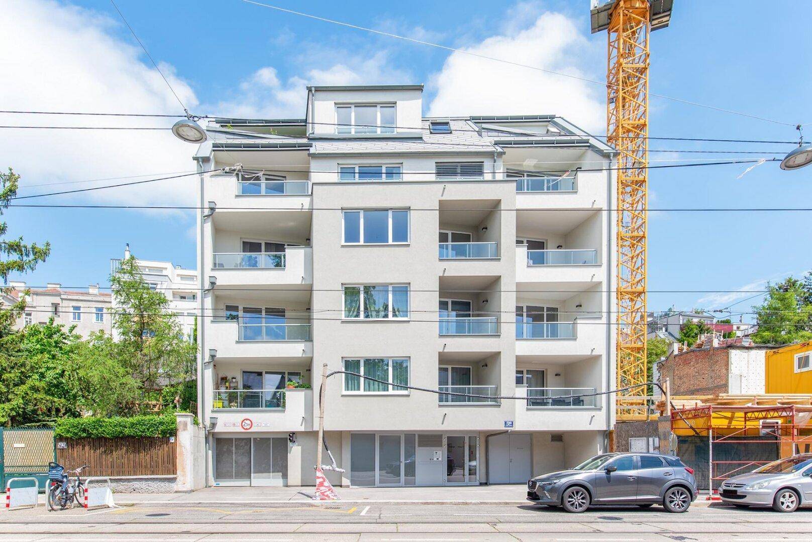 Modernes Mehrfamilienhaus mit mehreren Balkonen und großen Fenstern in städtischer Umgebung.