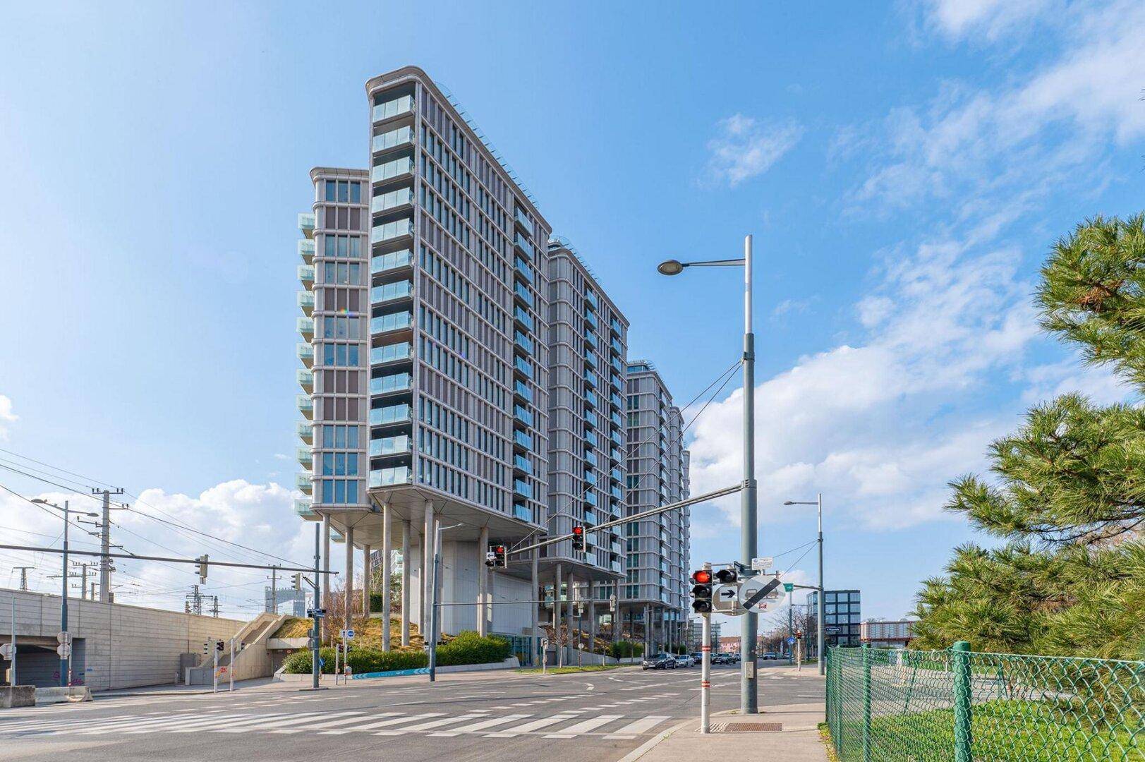 Moderne Hochhäuser mit vielen Balkonen und Glasfassaden an einer städtischen Straße.