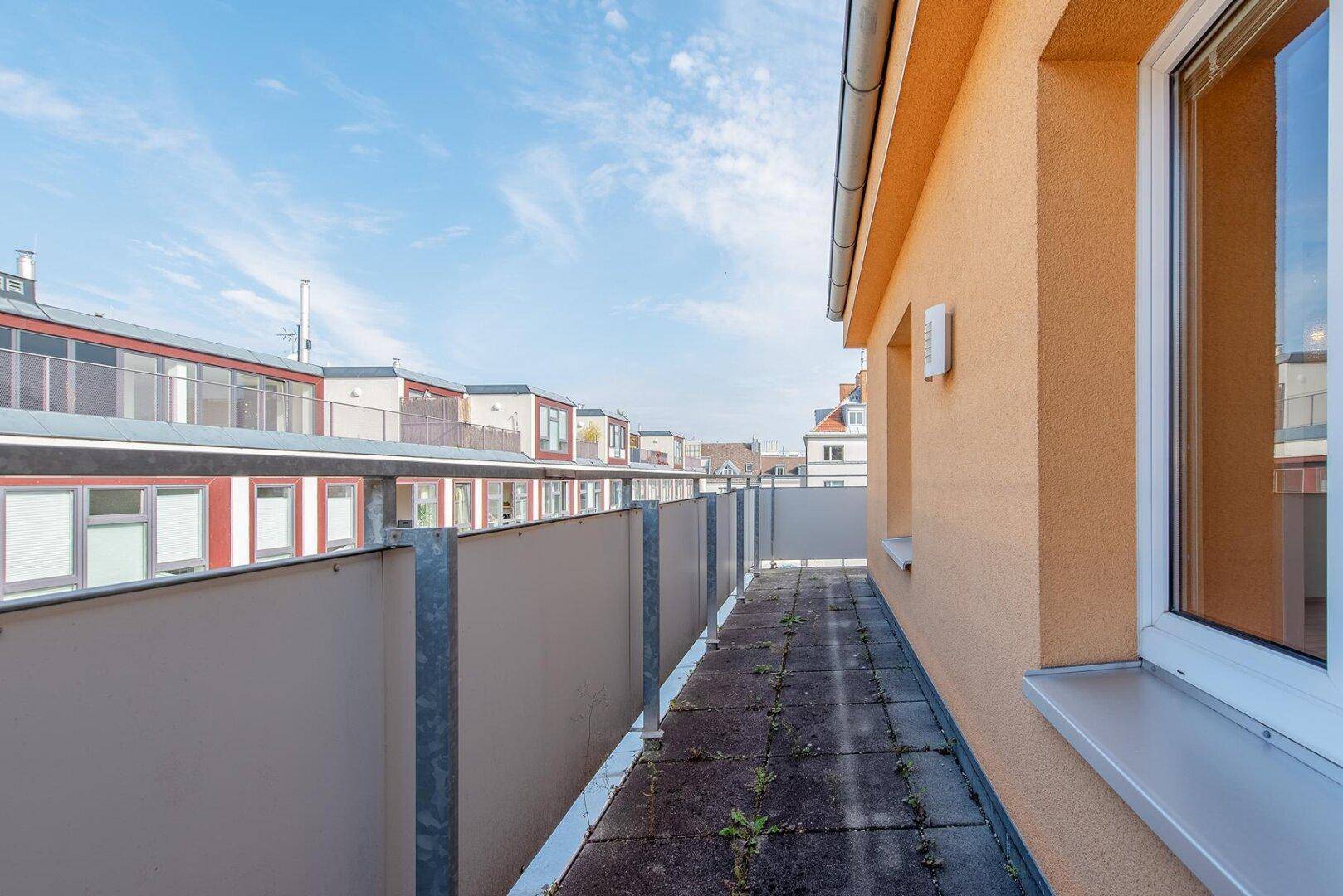 Lange, schmale Dachterrasse mit Fliesenboden und Blick auf die Nachbarschaft unter klarem Himmel.
