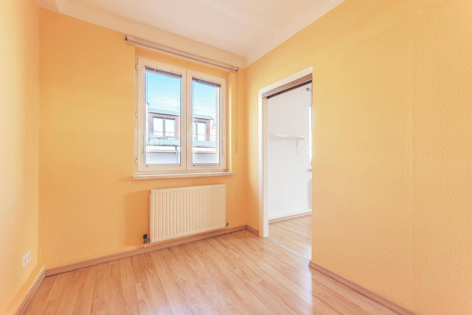 Helles Zimmer mit gelben Wänden, Laminatboden und einem Fenster mit Blick auf die Umgebung.