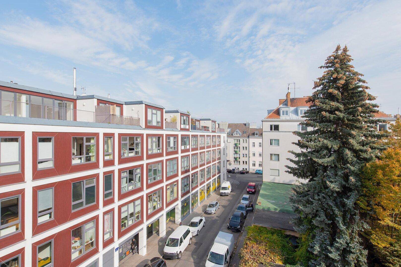 Blick von oben auf die Straße mit parkenden Autos und modernen Wohngebäuden in der Umgebung.