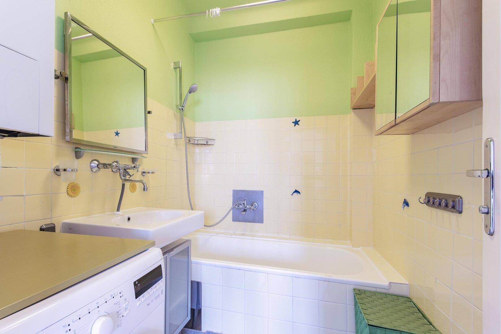 Badezimmer mit Badewanne, Waschbecken, gelben Fliesen und grün gestrichenen Wänden.