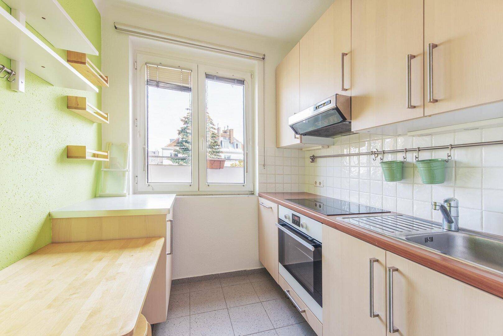 Funktionale Küche mit hellen Holzschränken, Fliesenboden und einem Fenster mit Ausblick.