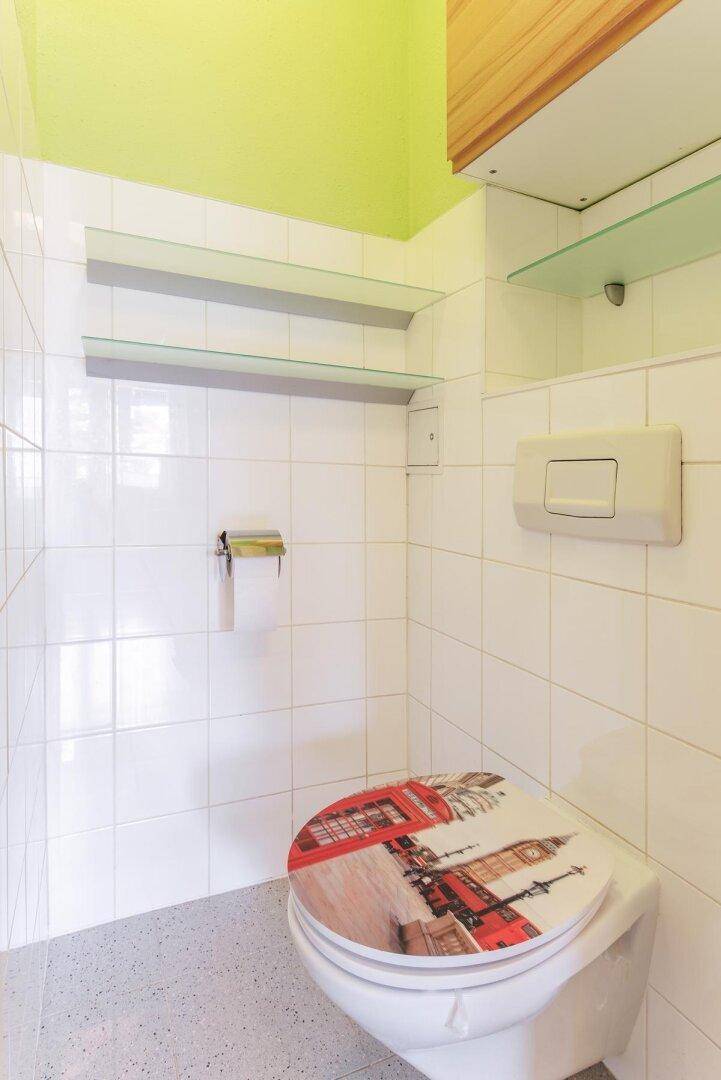 Separate Toilette mit weißen Fliesen, grün gestrichener Wand und einem Wand-WC.