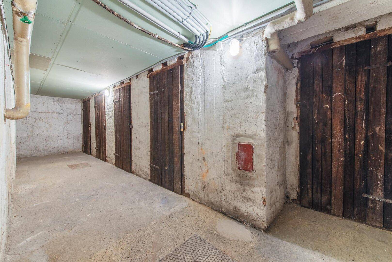 Kellerraum mit mehreren Holzabteilen, Betonboden und sichtbaren Rohren an der Decke.