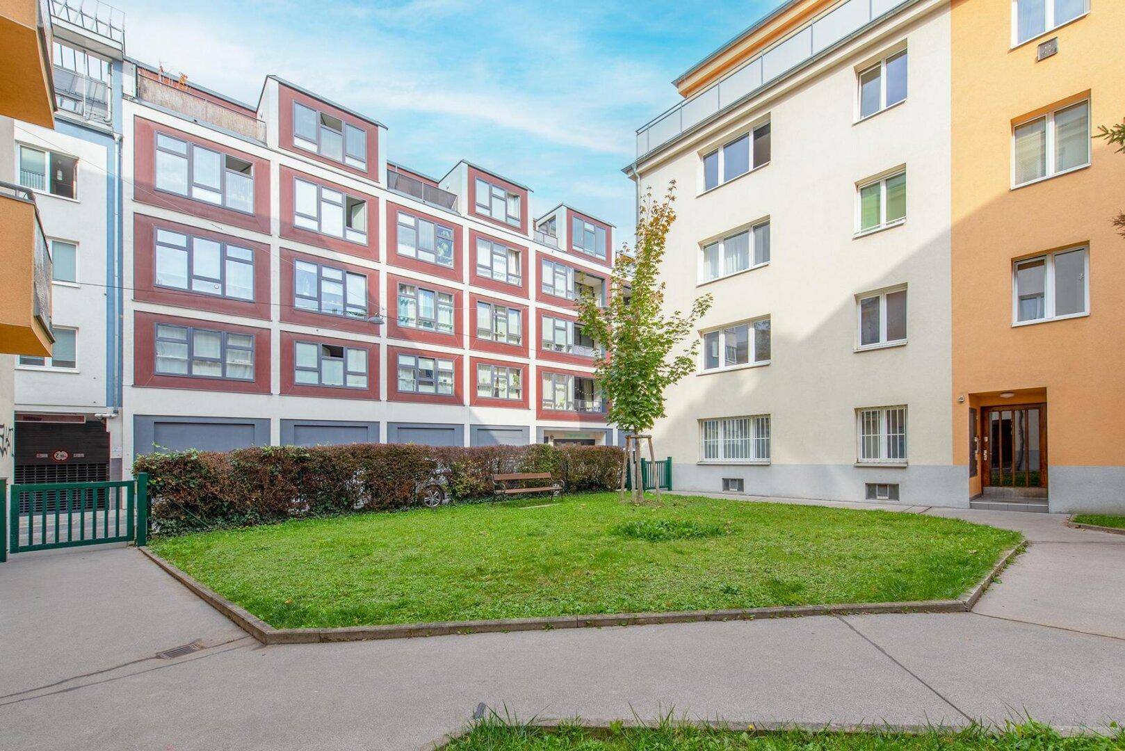 Gepflegter Gemeinschaftsgarten mit Rasenfläche und Sitzbank, umgeben von Wohngebäuden.