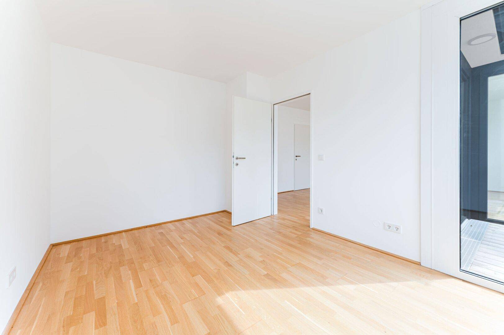 Leeres Zimmer mit Parkettboden und weiß gestrichenen Wänden, ideal für Schlafzimmer oder Büro.