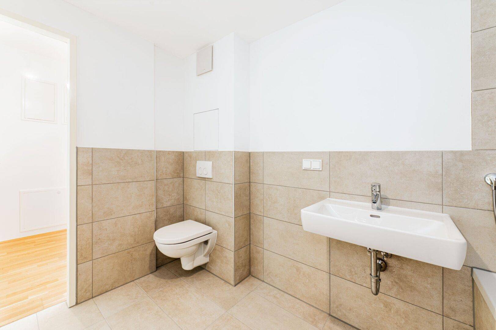 Helles Badezimmer mit beigefarbenen Fliesen, wandhängendem WC und modernem Waschbecken.