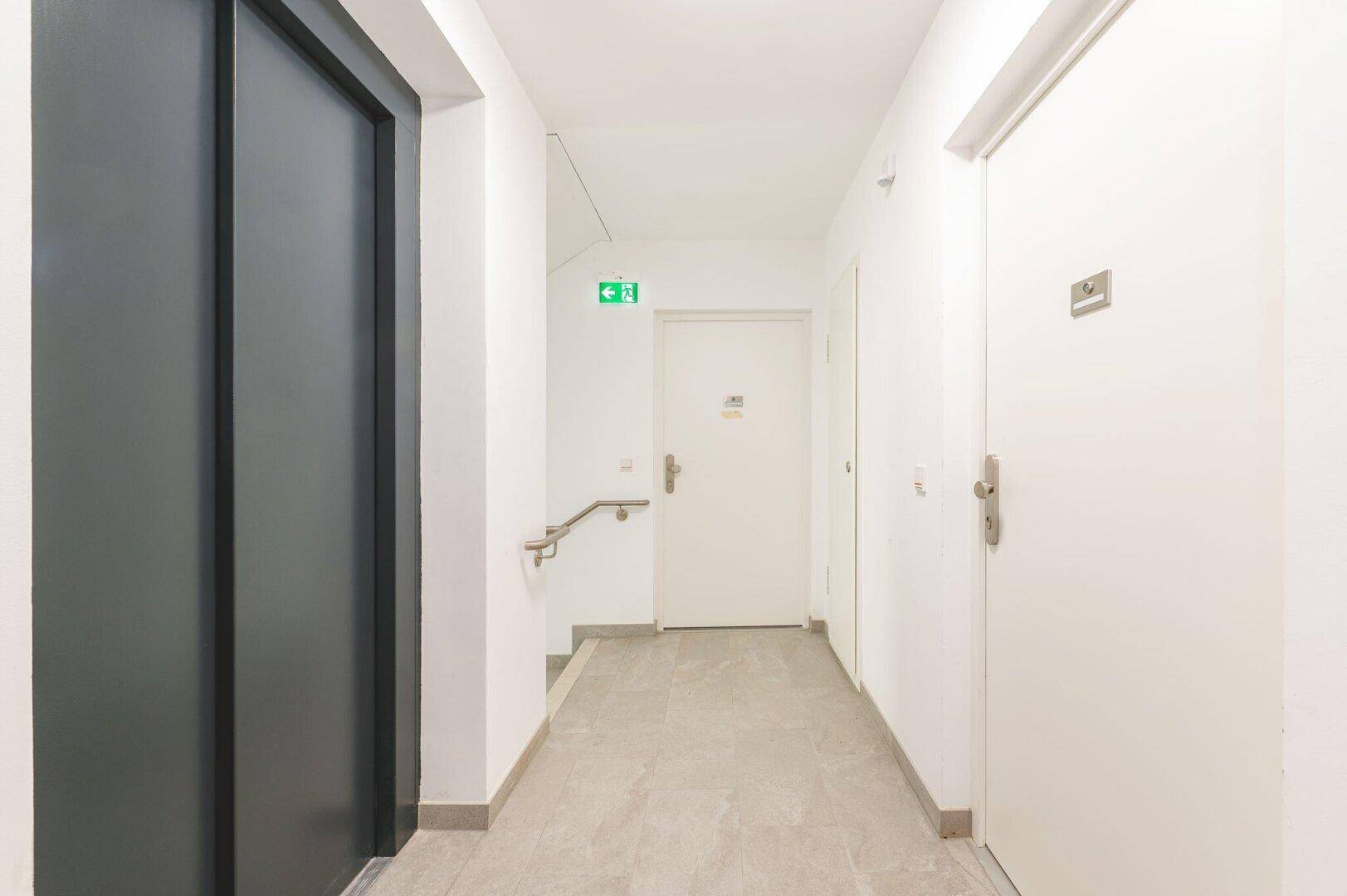 Heller Flur im Gebäude mit Aufzug, Treppe und Handläufen für Barrierefreiheit.