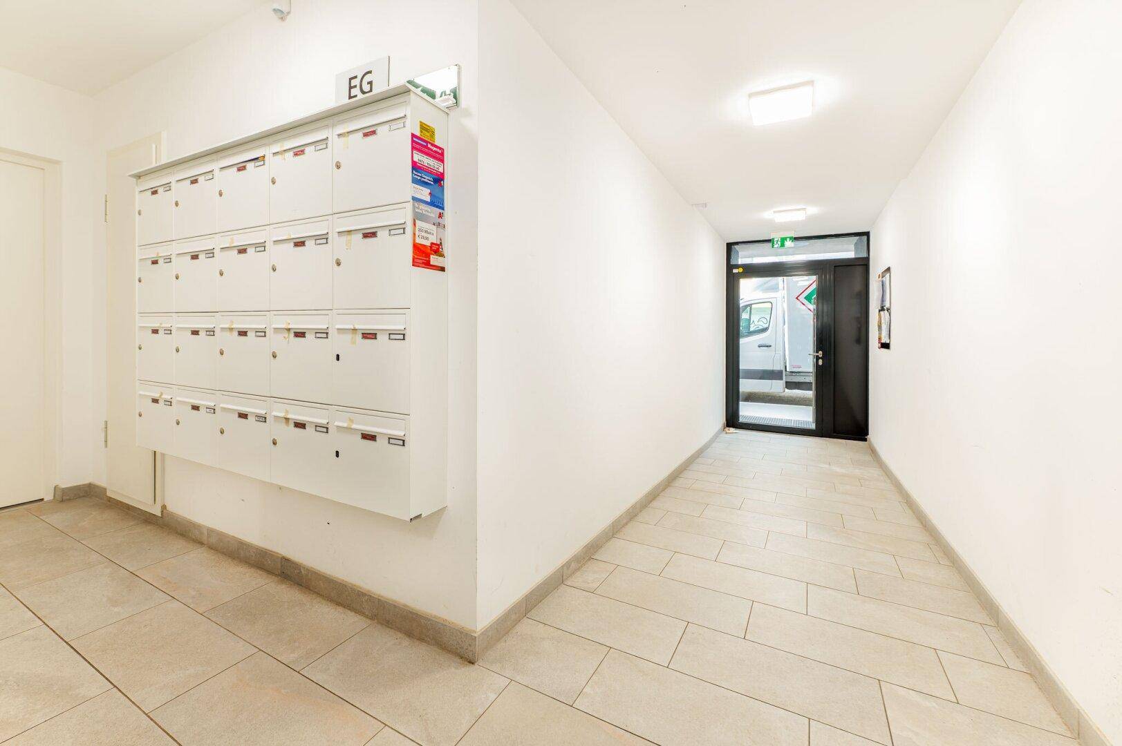 Langer, heller Flur im Erdgeschoss mit Briefkästen und Zugang zum Außenbereich.