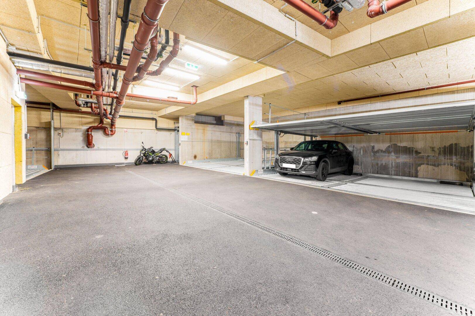 Tiefgarage mit mehreren Stellplätzen und sichtbaren Versorgungsleitungen an der Decke.