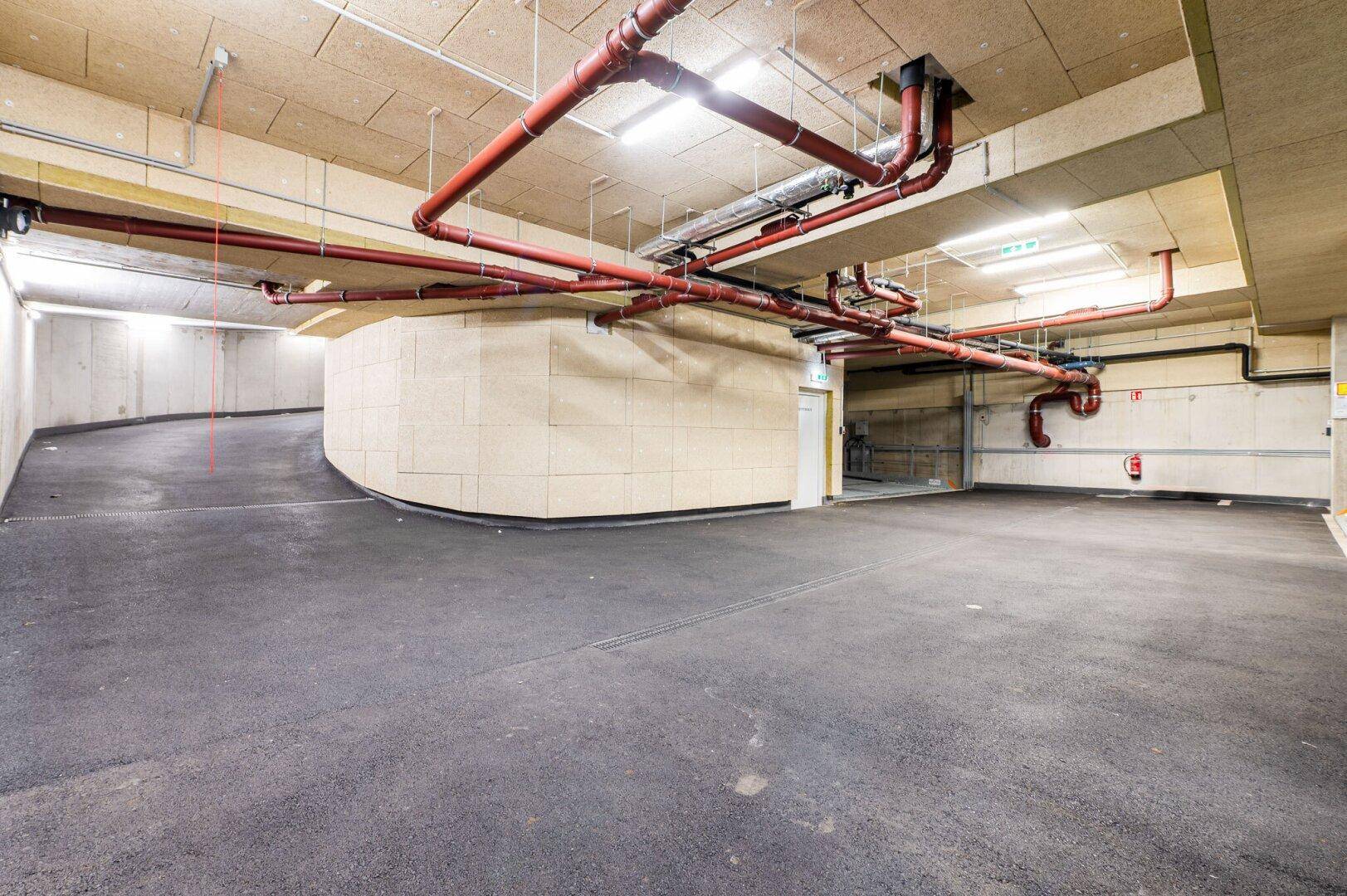 Zufahrt zur Tiefgarage mit Betonwänden und sichtbaren Rohrleitungen an der Decke.