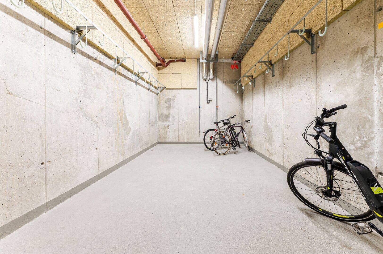 Fahrradraum im Keller mit Haken an der Wand und mehreren abgestellten Fahrrädern.