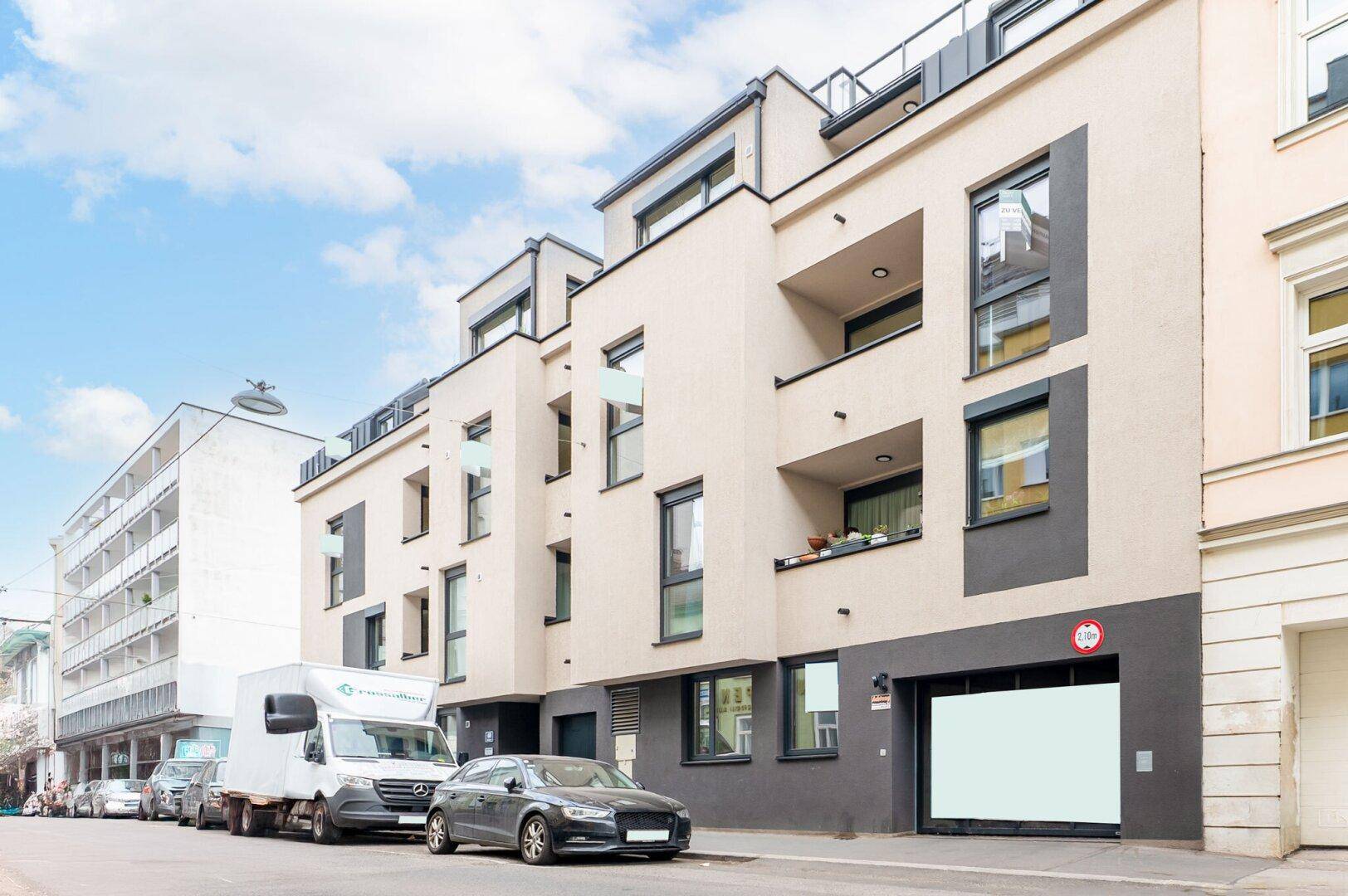 Moderne Wohnhausfassade mit Balkonen und großen Fenstern in städtischer Umgebung.