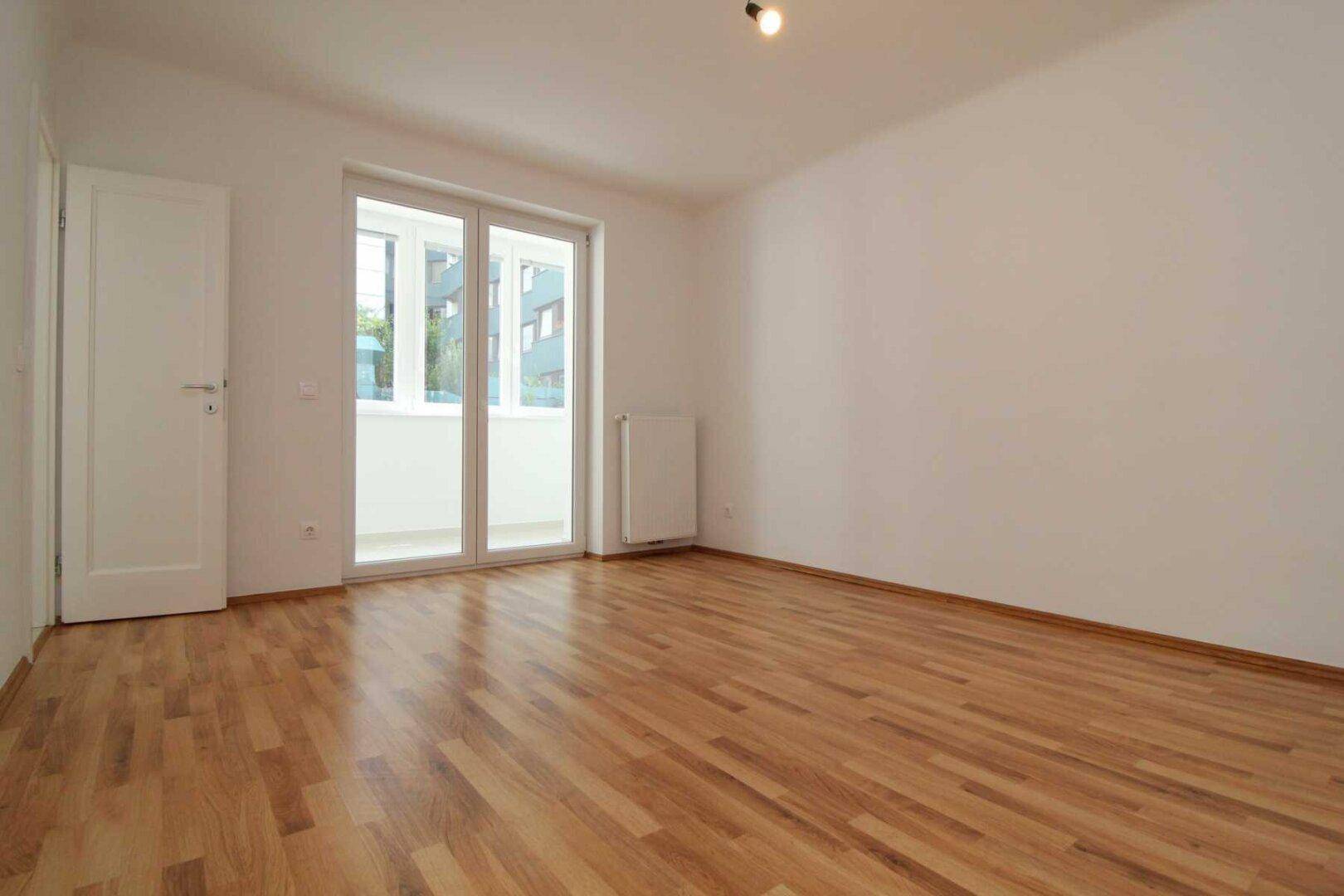 Lichtdurchflutetes Zimmer mit Holzboden und Zugang zu einem Balkon, bereit für individuelle Gestaltung.
