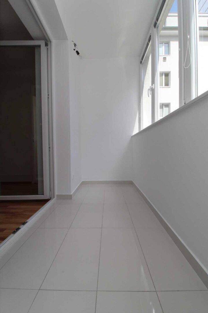 Langer, schmaler Balkon mit Fliesenboden und großen Fenstern, ideal für Entspannung im Freien.