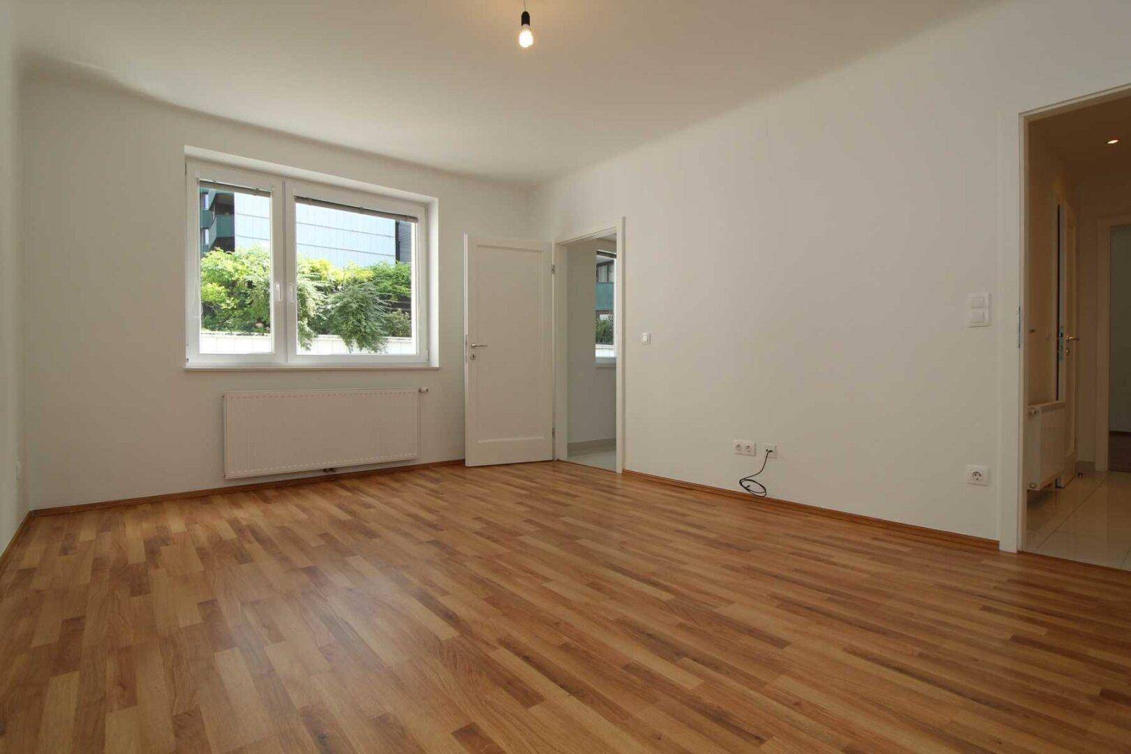 Geräumiges Schlafzimmer mit Parkettboden und großem Fenster, das viel natürliches Licht hereinlässt.