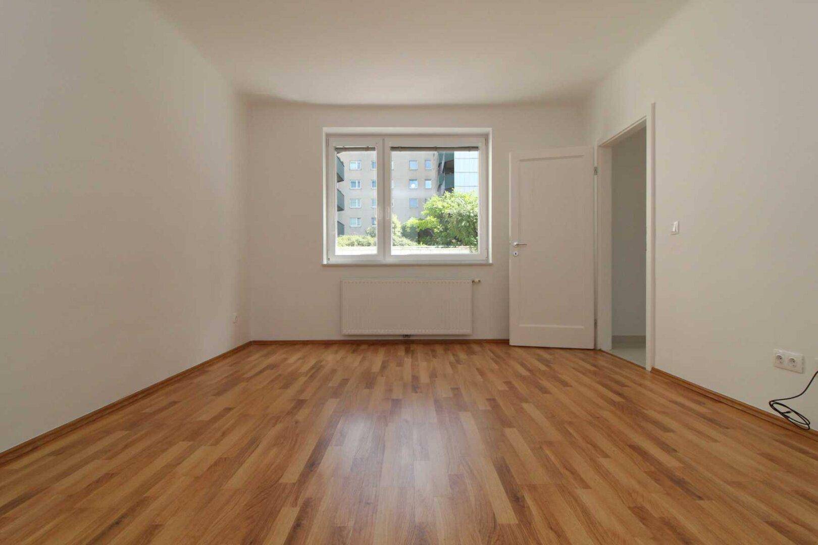 Helles Zimmer mit Parkettboden und Fensterblick auf die Umgebung, ideal als Schlaf- oder Arbeitszimmer.