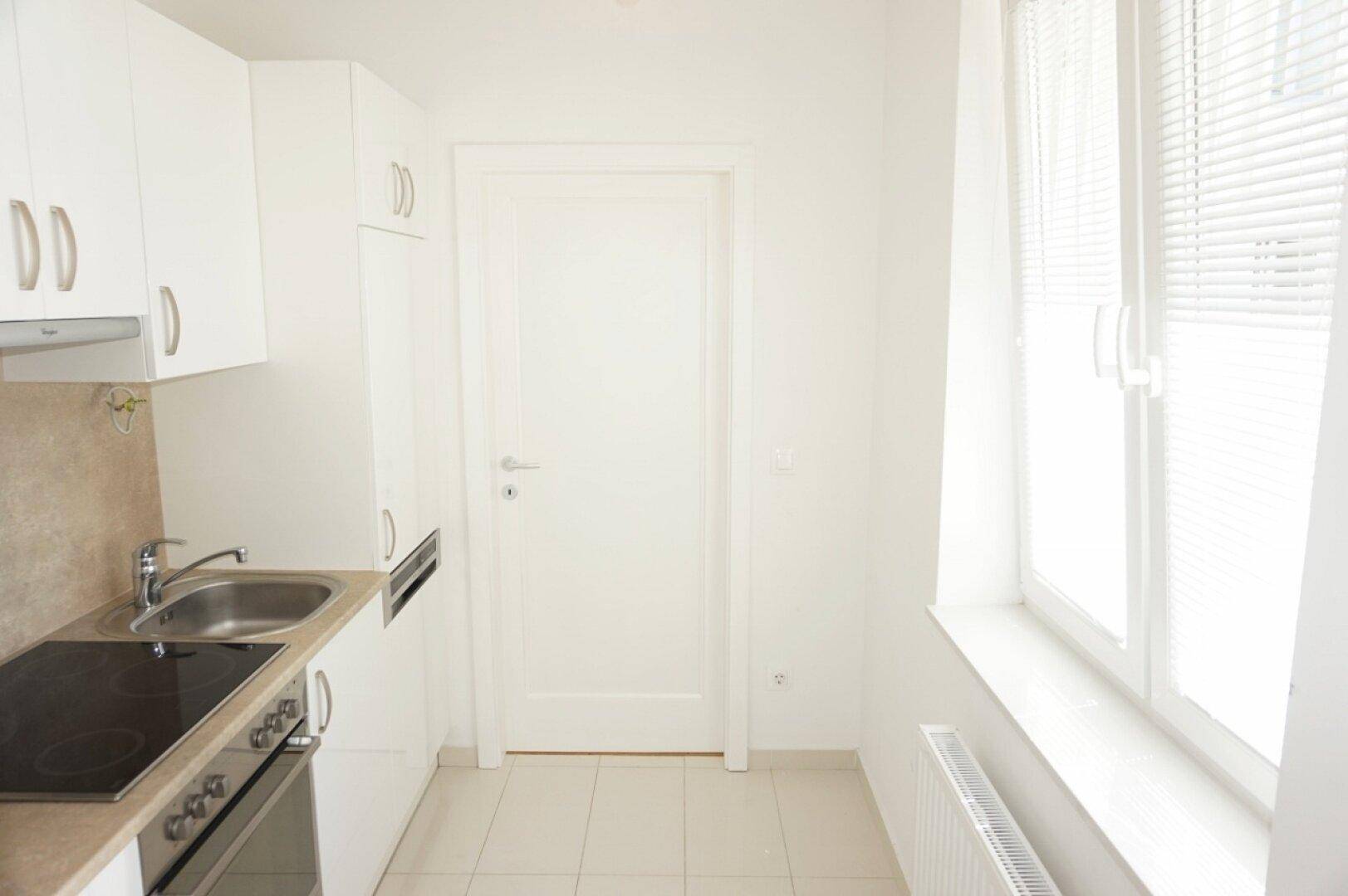 Kleine, helle Küche mit weißen Schränken, Spüle und Induktionskochfeld, ideal für kompaktes Wohnen.