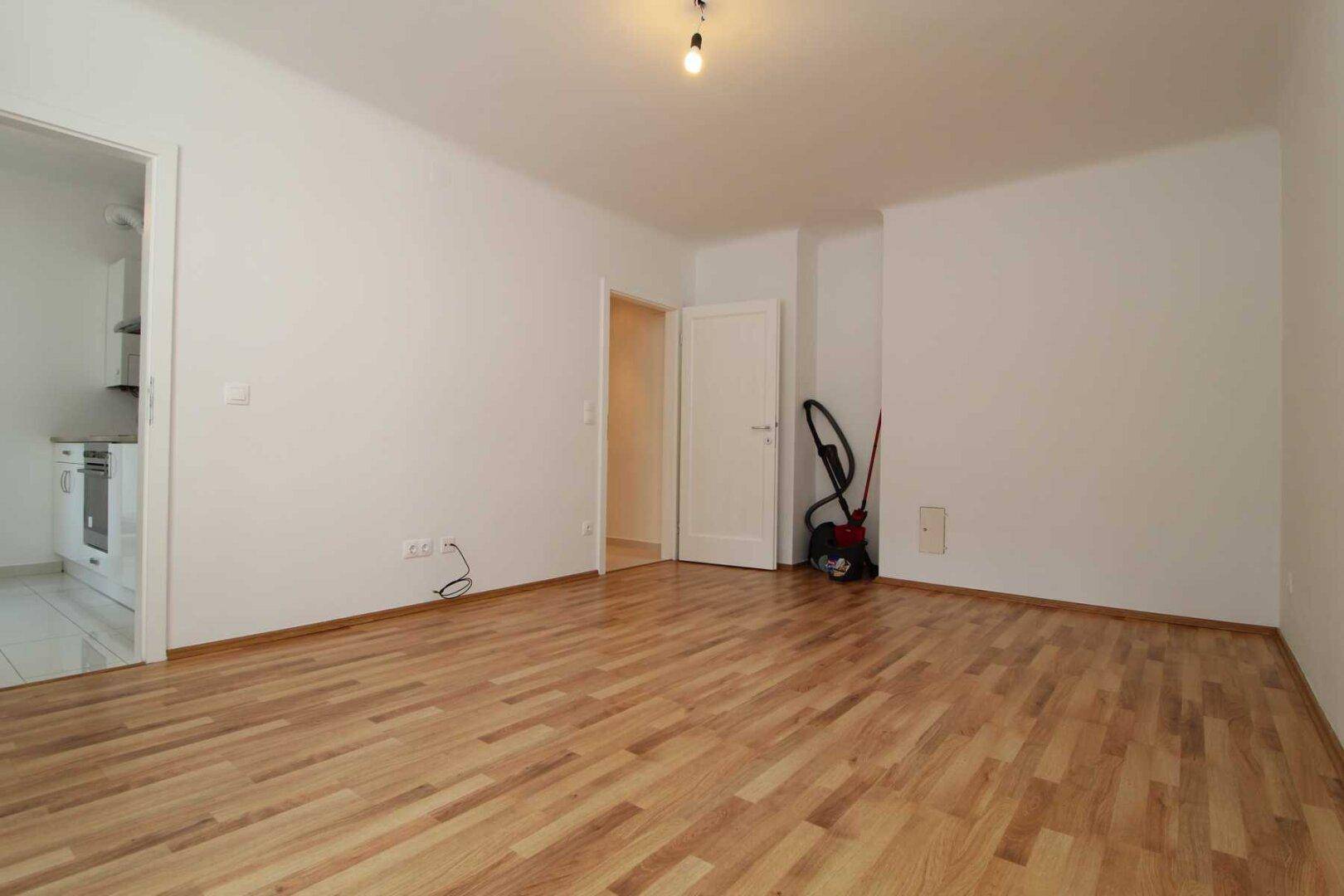 Heller Raum mit Parkettboden und Zugang zur Küche, vielseitig nutzbar als Wohn- oder Essbereich.