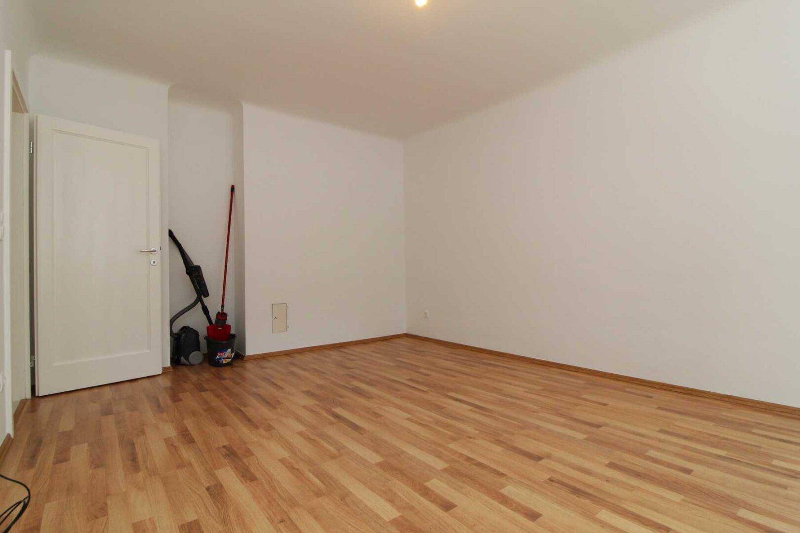 Leeres Zimmer mit Parkettboden und weißen Wänden, bietet flexible Nutzungsmöglichkeiten für Bewohner.