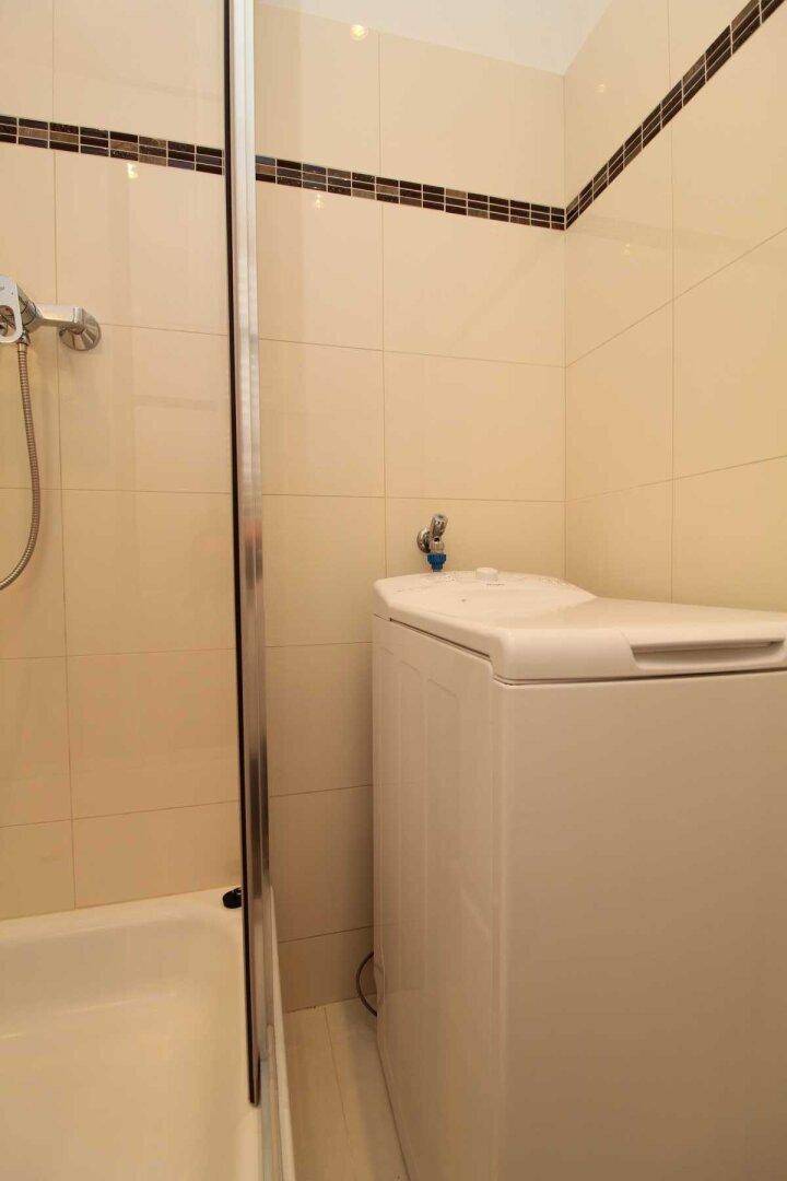 Duschbereich im Badezimmer mit Fliesen und einer praktischen Waschmaschine, effizient gestaltet.