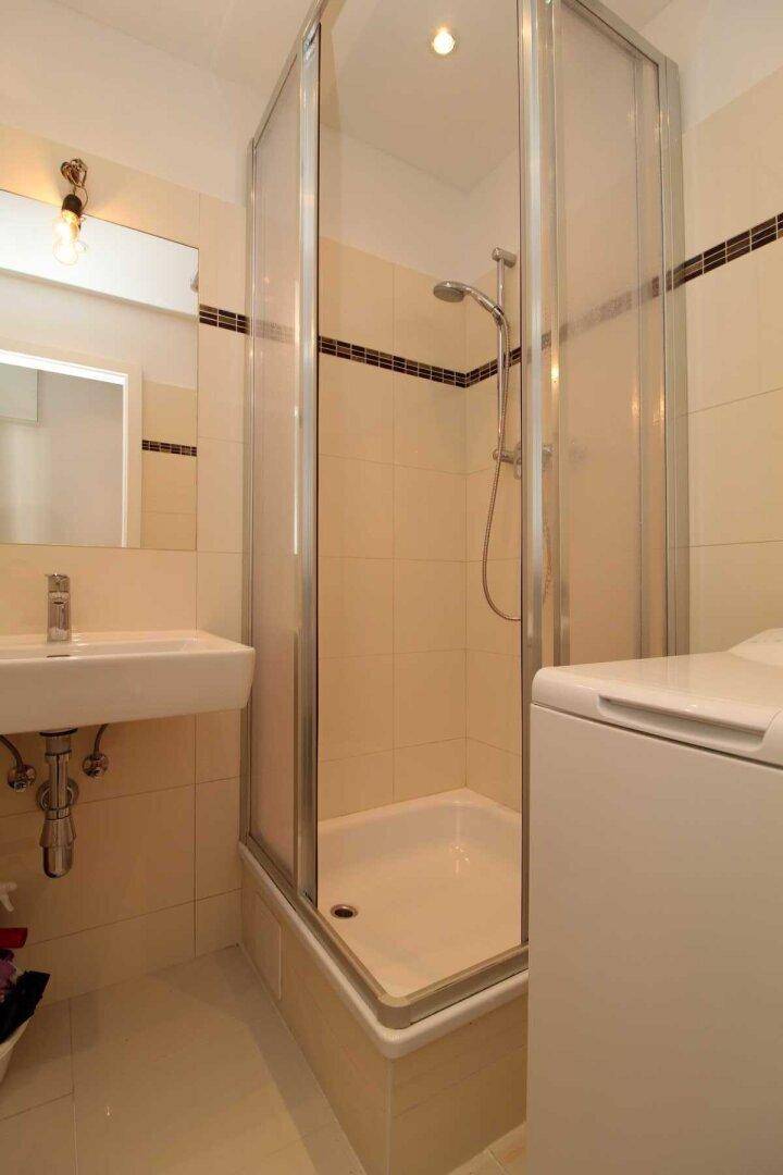 Modernes Badezimmer mit Duschkabine, Waschbecken und Waschmaschine, in hellen Beigetönen gefliest.