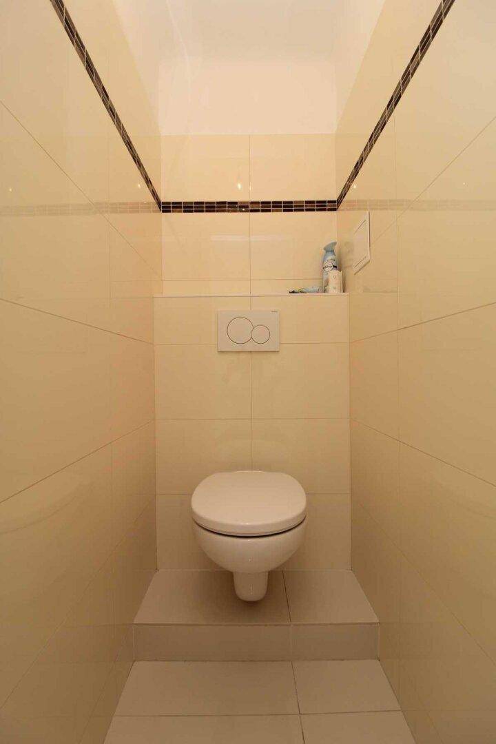 Separates WC mit wandhängender Toilette und hellen Fliesen, praktisch und pflegeleicht.