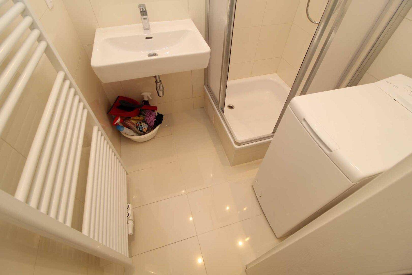 Kompaktes Badezimmer mit Dusche, Waschbecken, Waschmaschine und beheiztem Handtuchhalter, funktional eingerichtet.