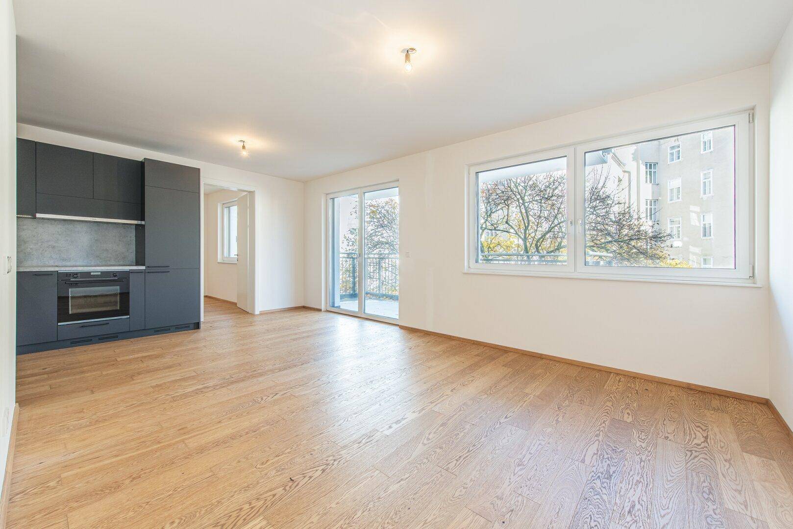 Lichtdurchfluteter Wohnbereich mit großen Fenstern und Zugang zum Balkon.
