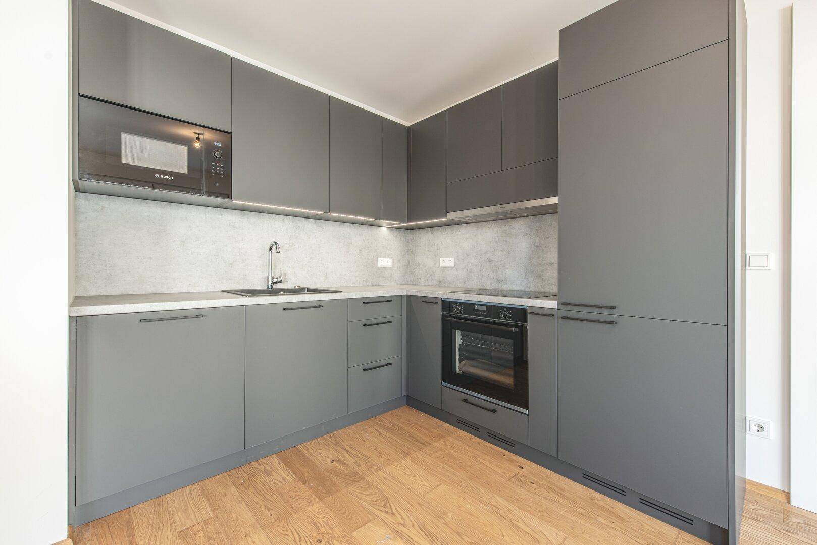 Moderne Küchenzeile in Grau mit integrierten Geräten und Mikrowelle.