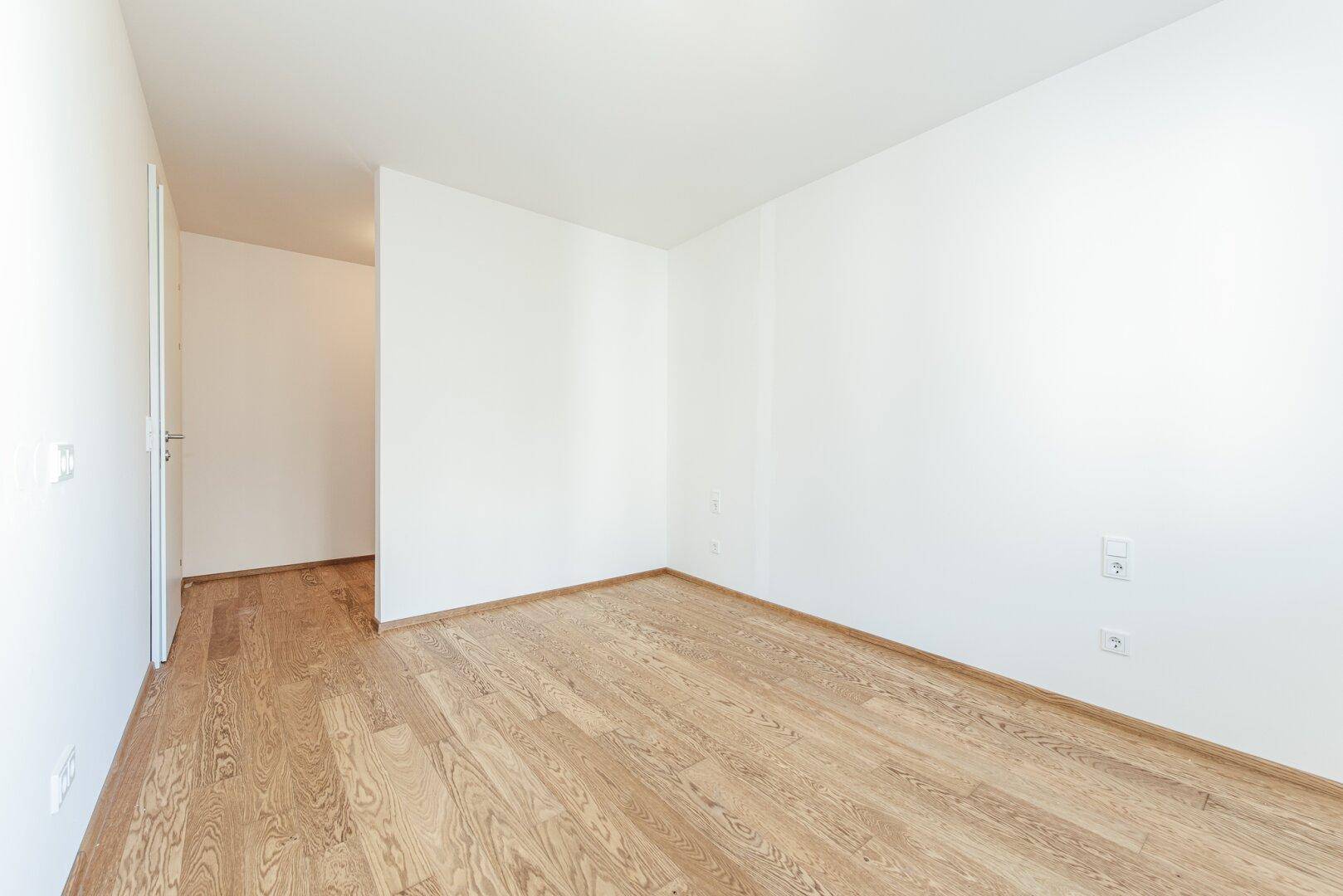 Leeres Schlafzimmer mit hellem Parkettboden und weißen Wänden, bereit zum Einzug.