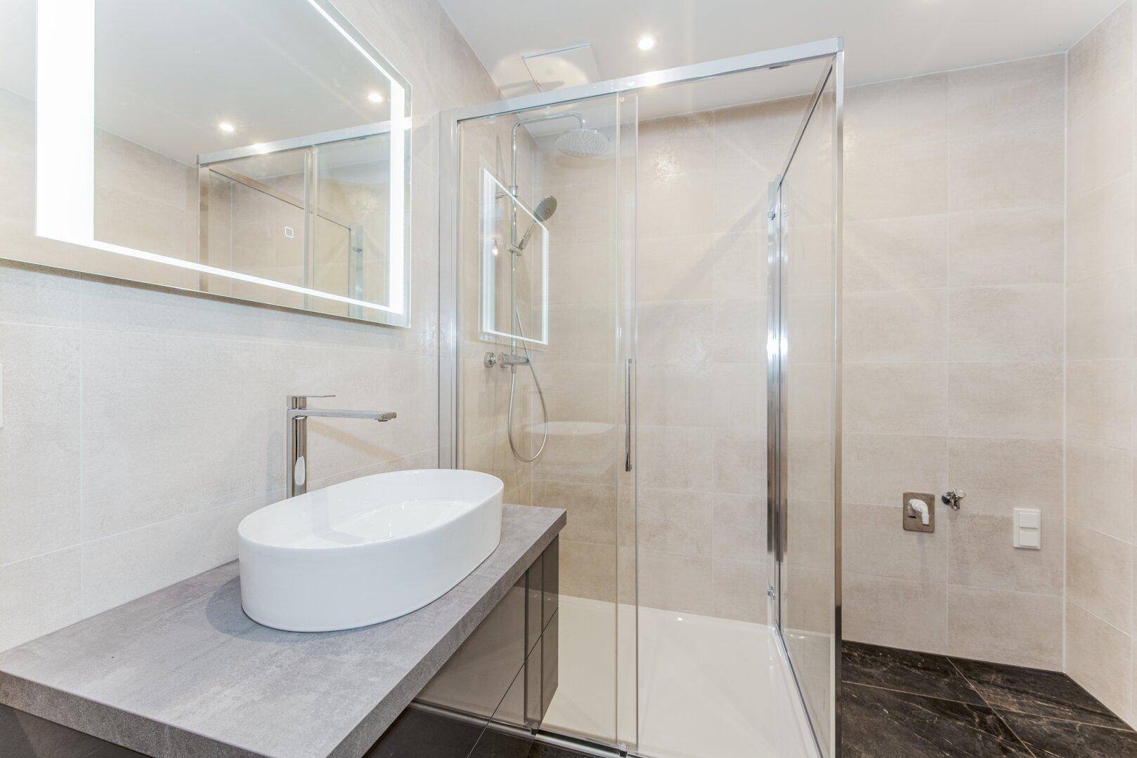 Modernes Badezimmer mit begehbarer Dusche, eleganten Fliesen und beleuchtetem Spiegel.