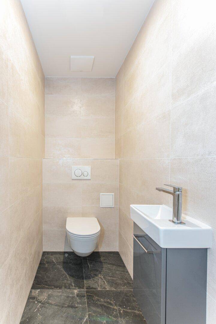 Modernes Gäste-WC mit Wand-WC, kleinem Waschbecken und dunklem Fliesenboden.