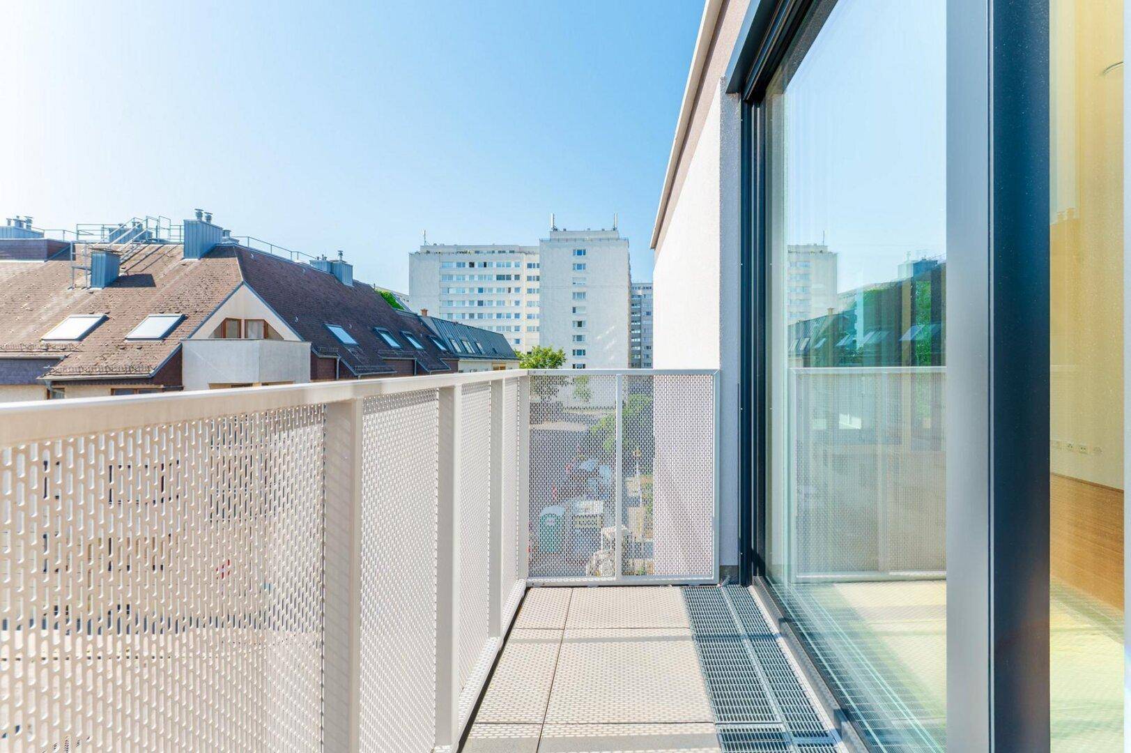Heller Balkon mit Fliesenboden und modernem Geländer, bietet einen weiten Blick über die Stadt.