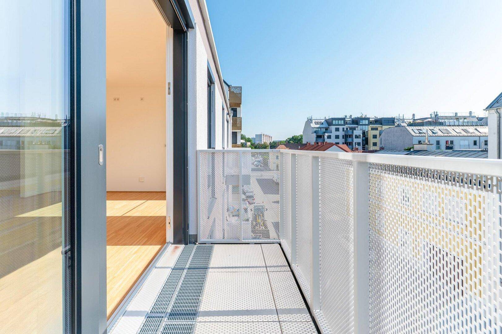 Moderner Balkon mit perforiertem Geländer und Blick auf die Stadtstraße und umliegende Gebäude.