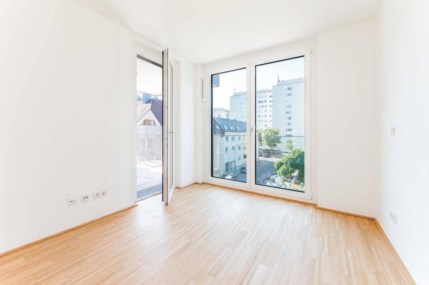 Helles Zimmer mit Parkettboden und großem Fenster, das einen angenehmen Blick ins Grüne bietet.