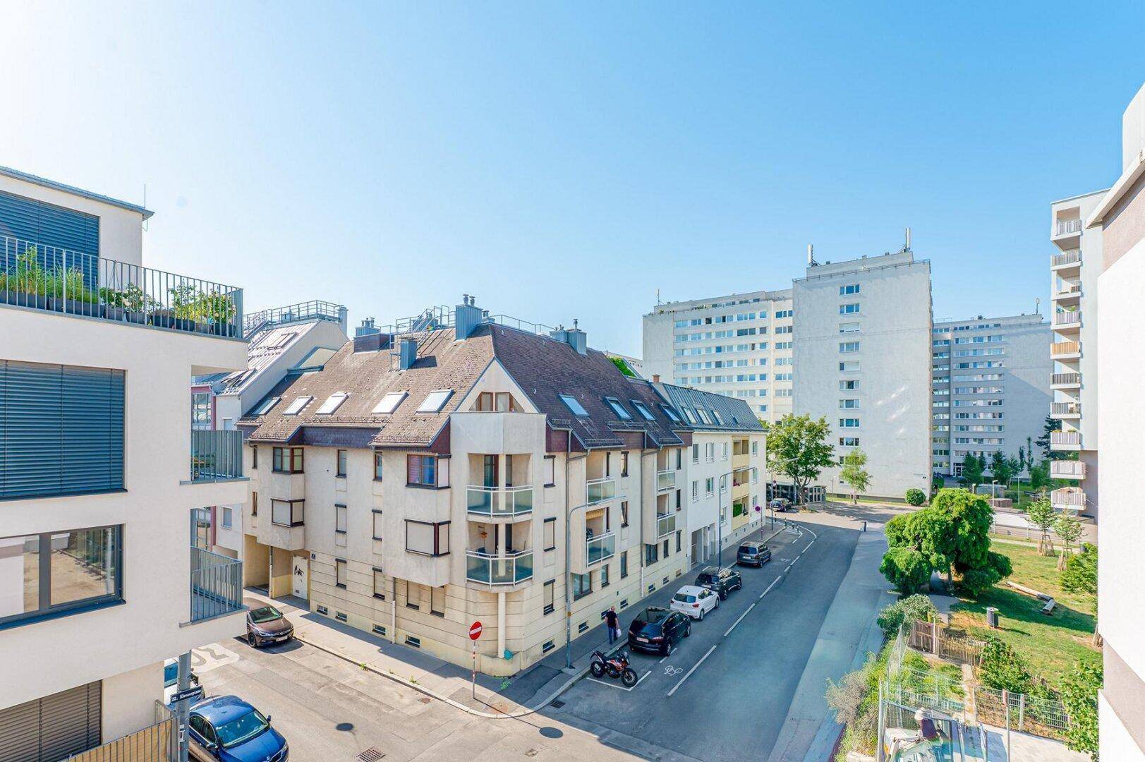 Panoramablick über eine städtische Straße mit verschiedenen Gebäudetypen unter blauem Himmel.