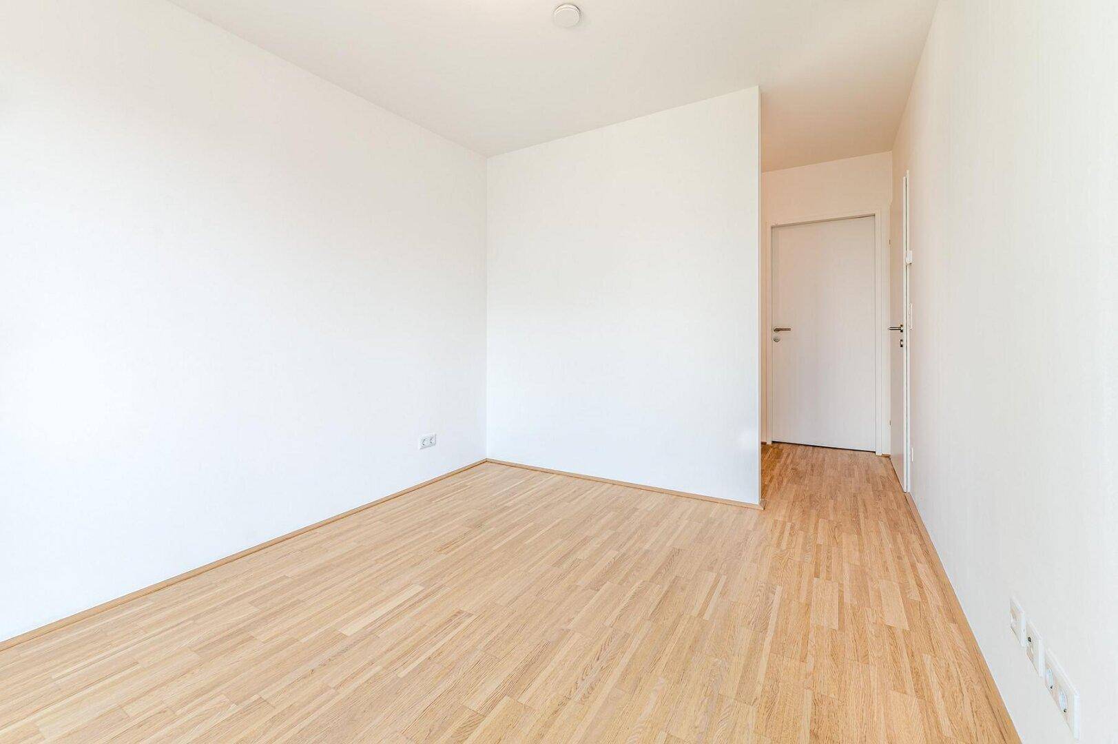 Schlichter, heller Raum mit Parkettboden und weißen Wänden, ideal als Schlaf- oder Arbeitszimmer.