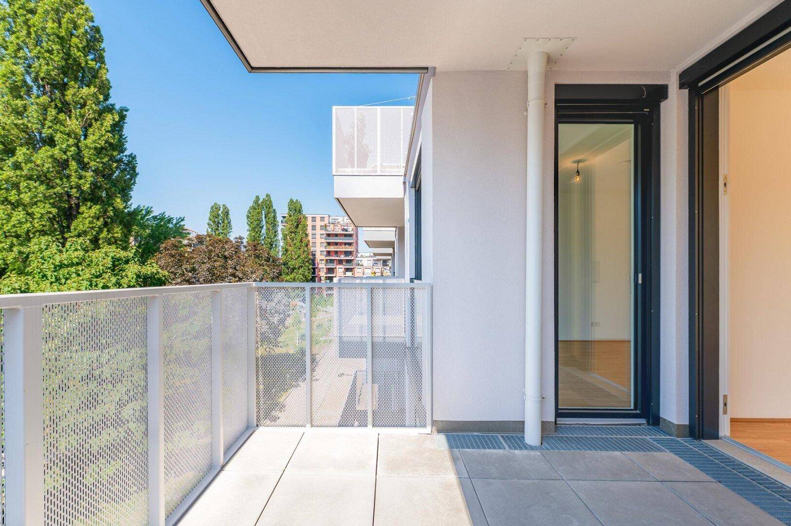 Geräumiger Balkon mit Fliesenboden und Blick auf grüne Bäume und die umliegende Bebauung.