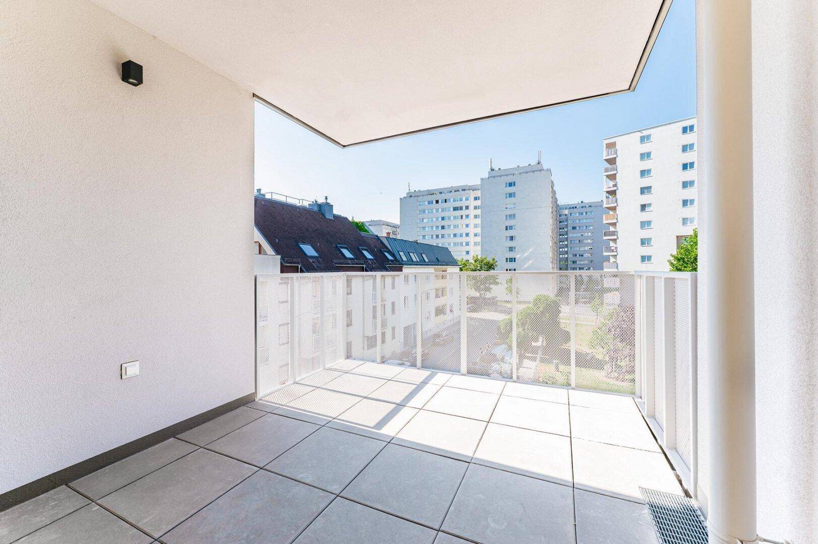 Heller Balkon mit Fliesenboden und weitem Blick über die Dächer der Stadt und die Straße.