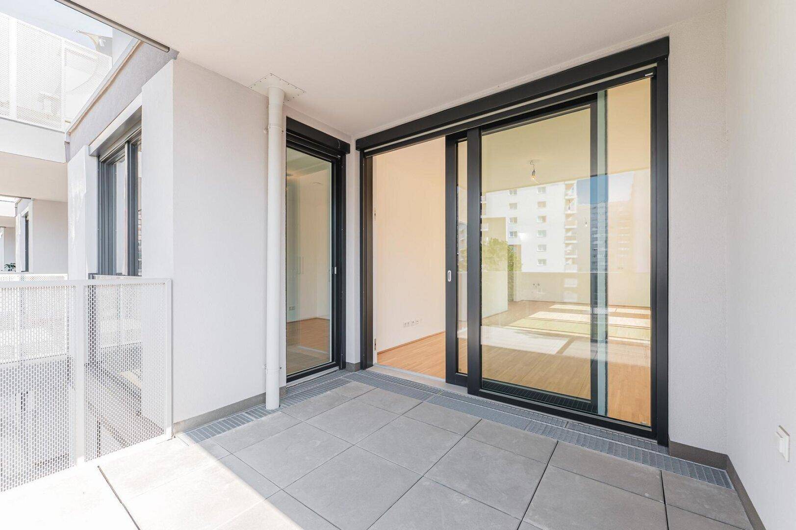 Moderner Balkon mit Fliesenboden und großen Schiebetüren, die den Innenraum mit dem Außenbereich verbinden.