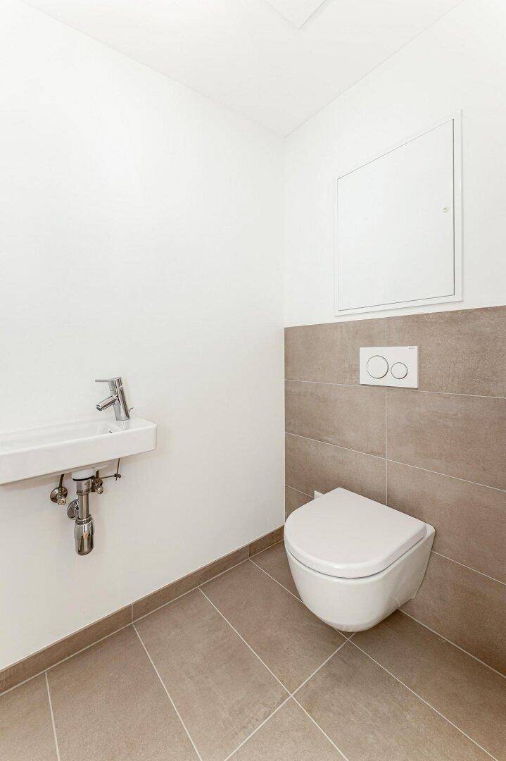 Modernes Gäste-WC mit wandhängender Toilette und kleinem Waschbecken in neutralen Farbtönen.