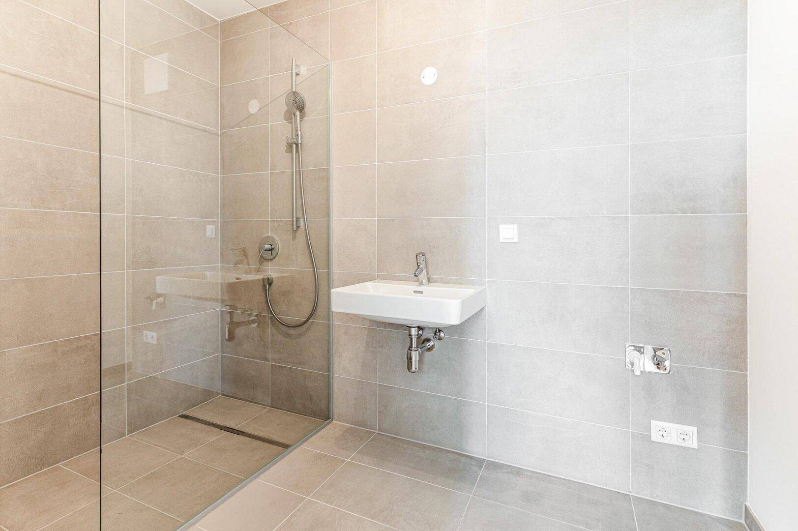 Helles Badezimmer mit großen Fliesen, ebenerdiger Dusche und modernem Waschbecken.