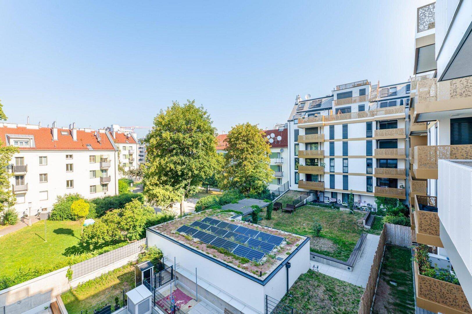 Innenhof mit grünen Gärten, Bäumen und einem Gebäude mit Photovoltaikanlage auf dem Dach.