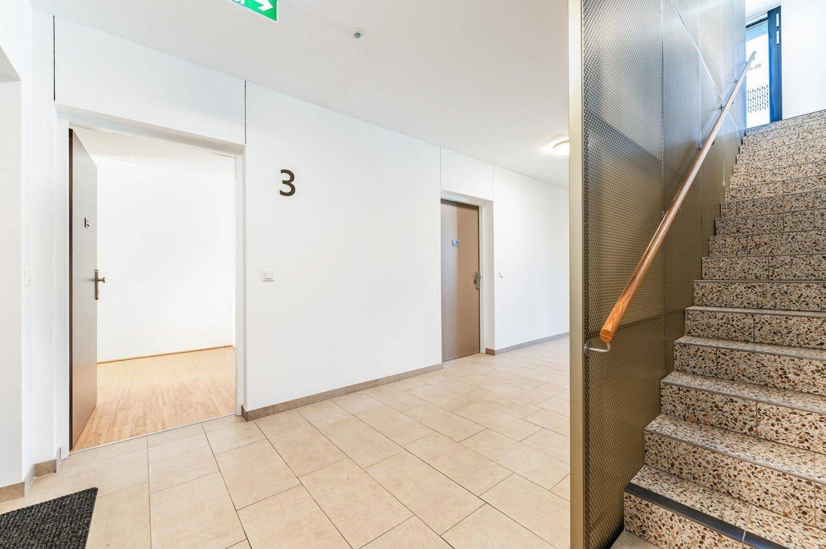 Heller Flur mit Treppenaufgang und Zugang zu den Wohneinheiten in einem modernen Gebäude.